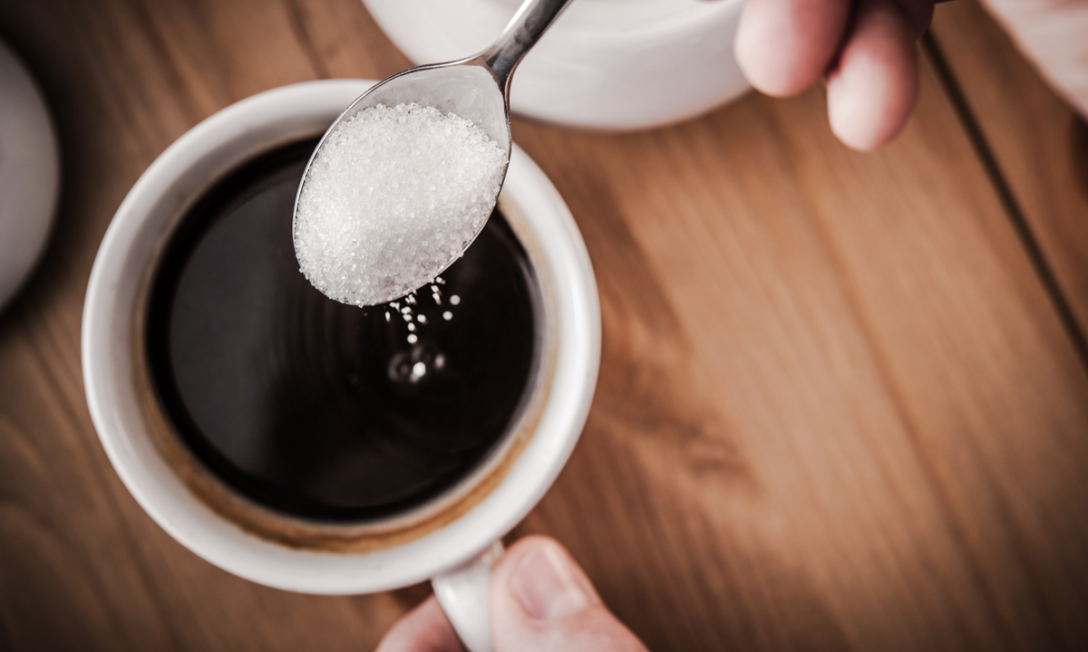 Spooning sugar into a coffee cup