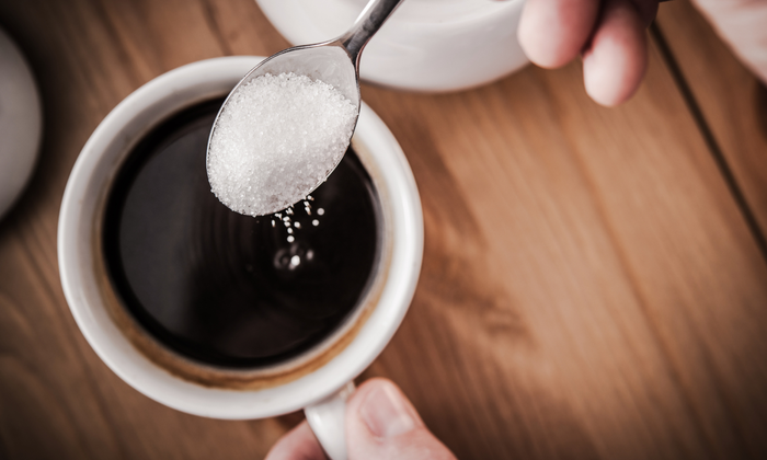 Spooning sugar into a coffee cup